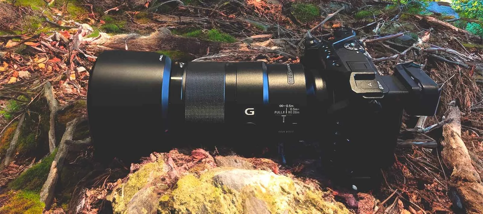 Sony Alpha camera with FE 2.8 G macro lens lying on a mossy forest floor