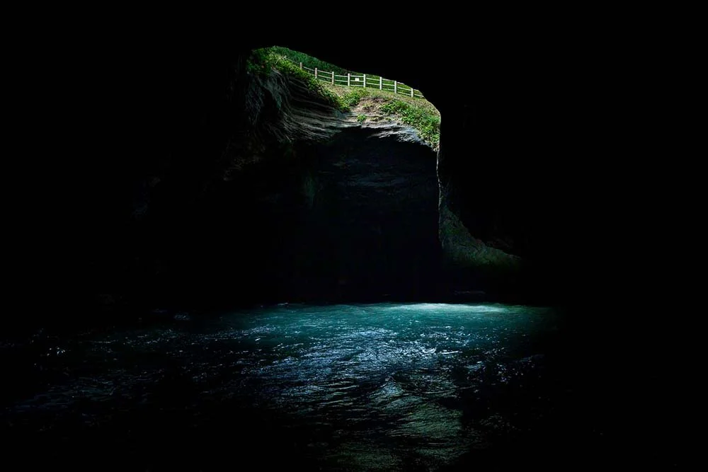Daylight falling through the ceiling opening of Tensodo sea cave onto glowing turquoise water, Dogashima, Izu, Japan.