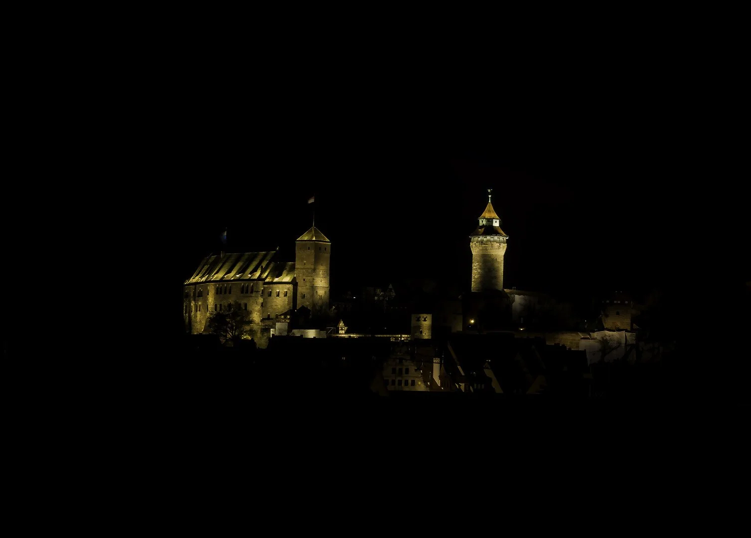 Die beleuchtete Kaiserburg Nürnberg hebt sich nachts scharf vom dunklen Himmel ab.