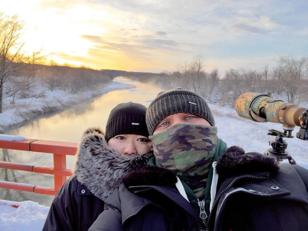 Markus Nilles et une accompagnatrice sur un pont enneigé au lever du soleil, longue-vue à l’arrière-plan.