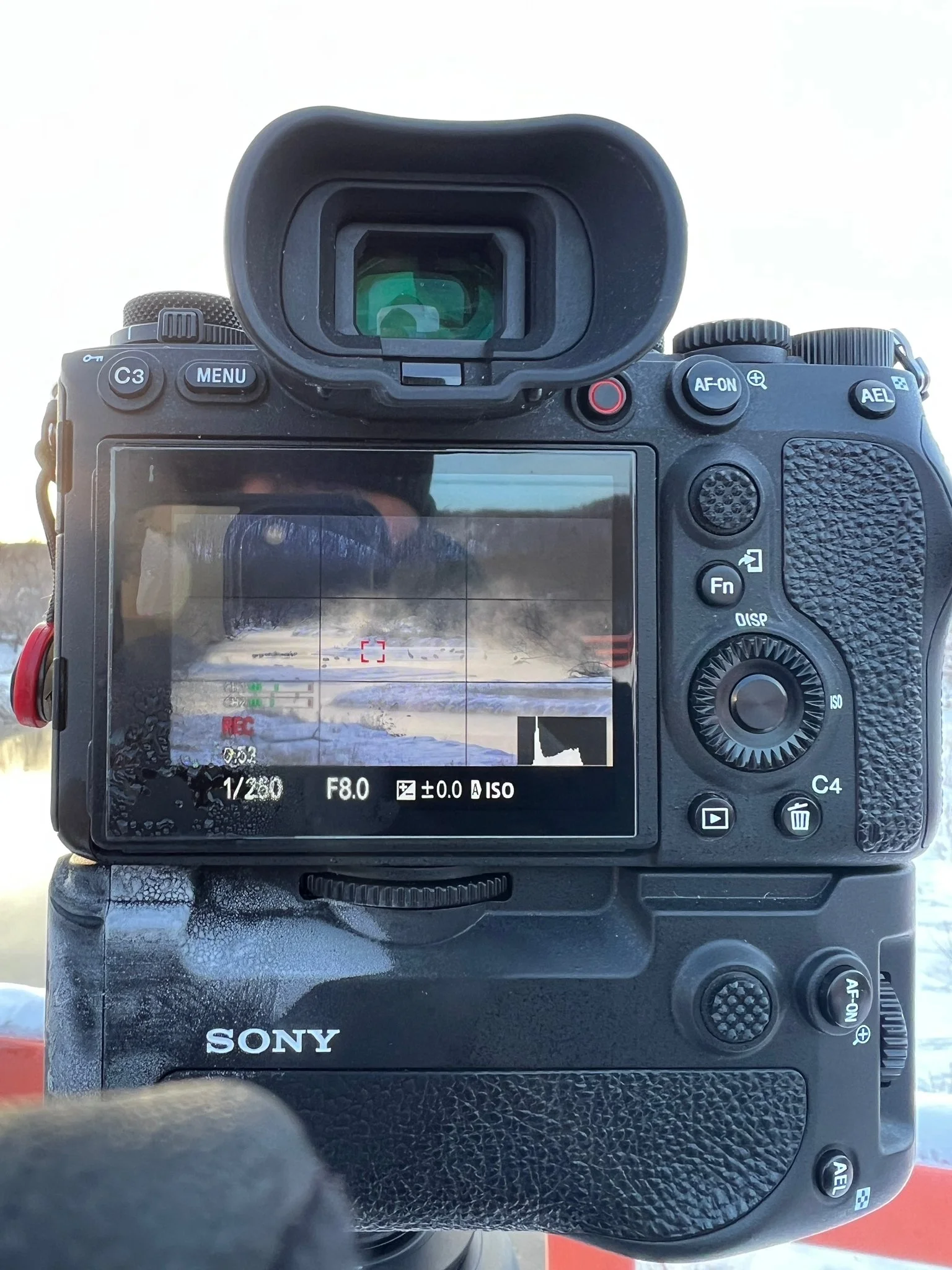 Sony camera back displaying a live view of a snowy, steaming river landscape.